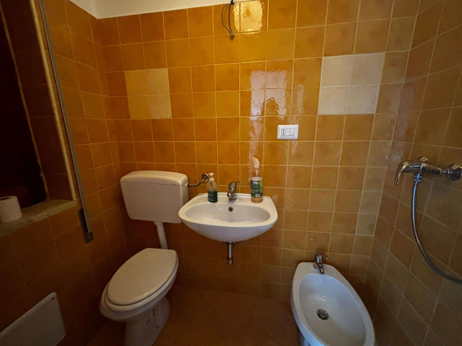 Vaschetta bagno e bidet in un bagno con piastrelle arancioni, impianto idraulico visibile, ideale per ristrutturazioni e arredamento di case in vendita o affitto.