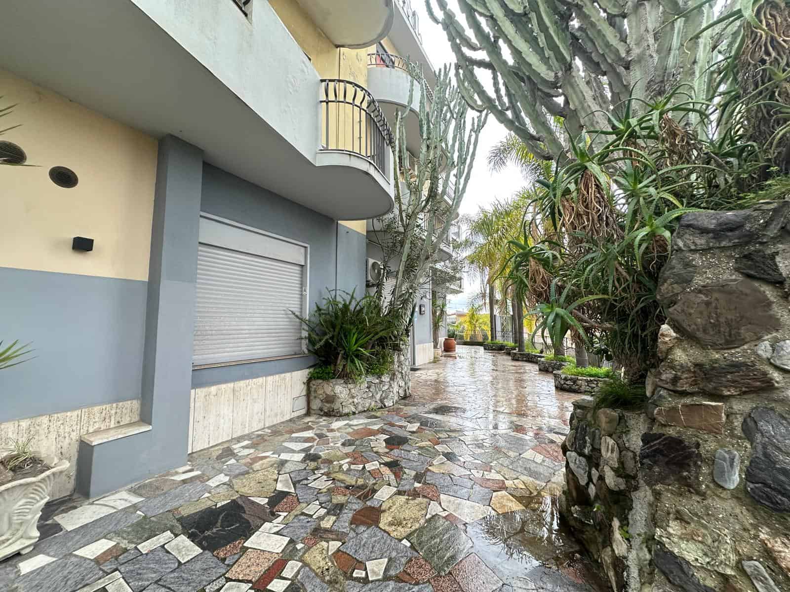 Elegante vialetto condominiale con pavimentazione in pietra naturale e piante tropicali, ideale per un contesto residenziale di alto livello.