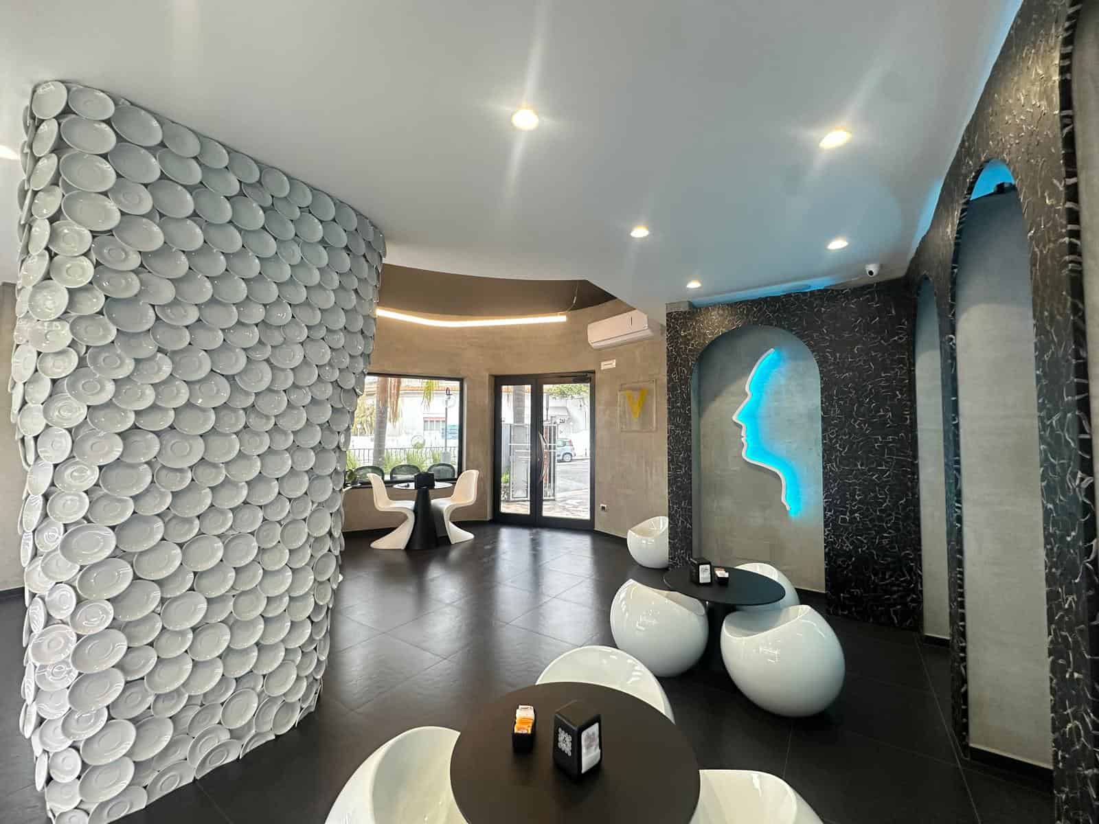 1. Interno moderno con parete decorativa a forma di profilo umano illuminato e sedute di design bianche e nere.