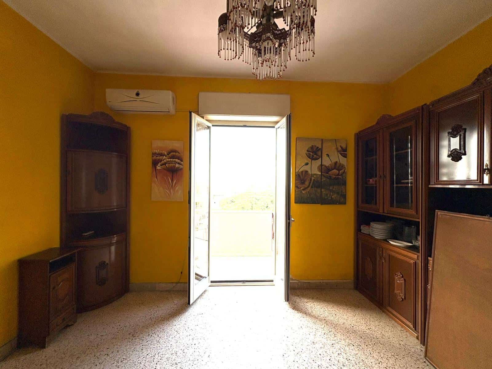 Balcone luminoso in appartamento con pareti gialle e mobili in legno, ideale per vivere e arredare con stile. Servizio di agenzia immobiliare NextCasa, vendita e affitti immobili vicino a te.