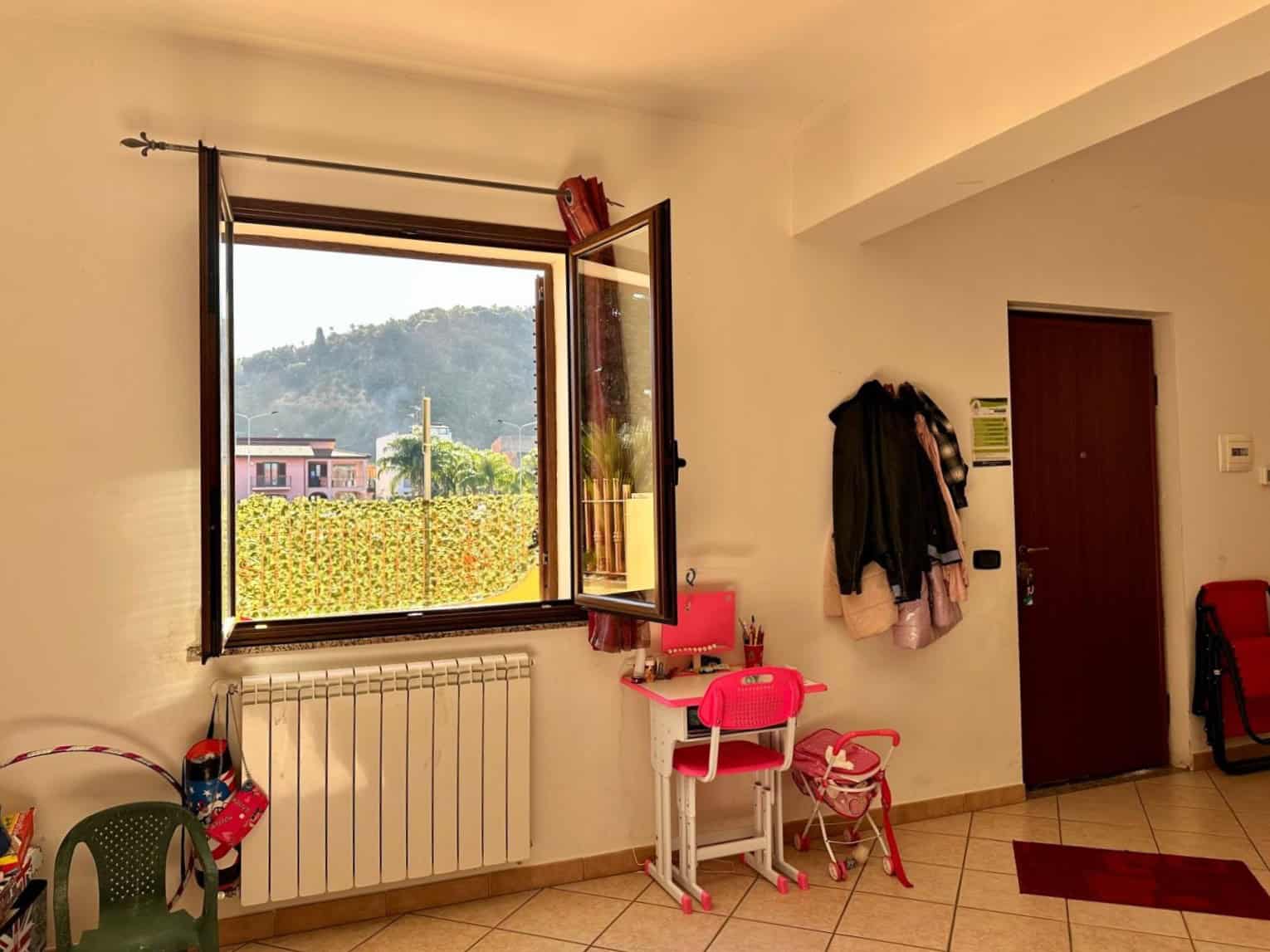 1. Finestra aperta con vista su collina e case, ambiente interno luminoso, arredamento per bambini, ingresso appartamento, stile moderno.