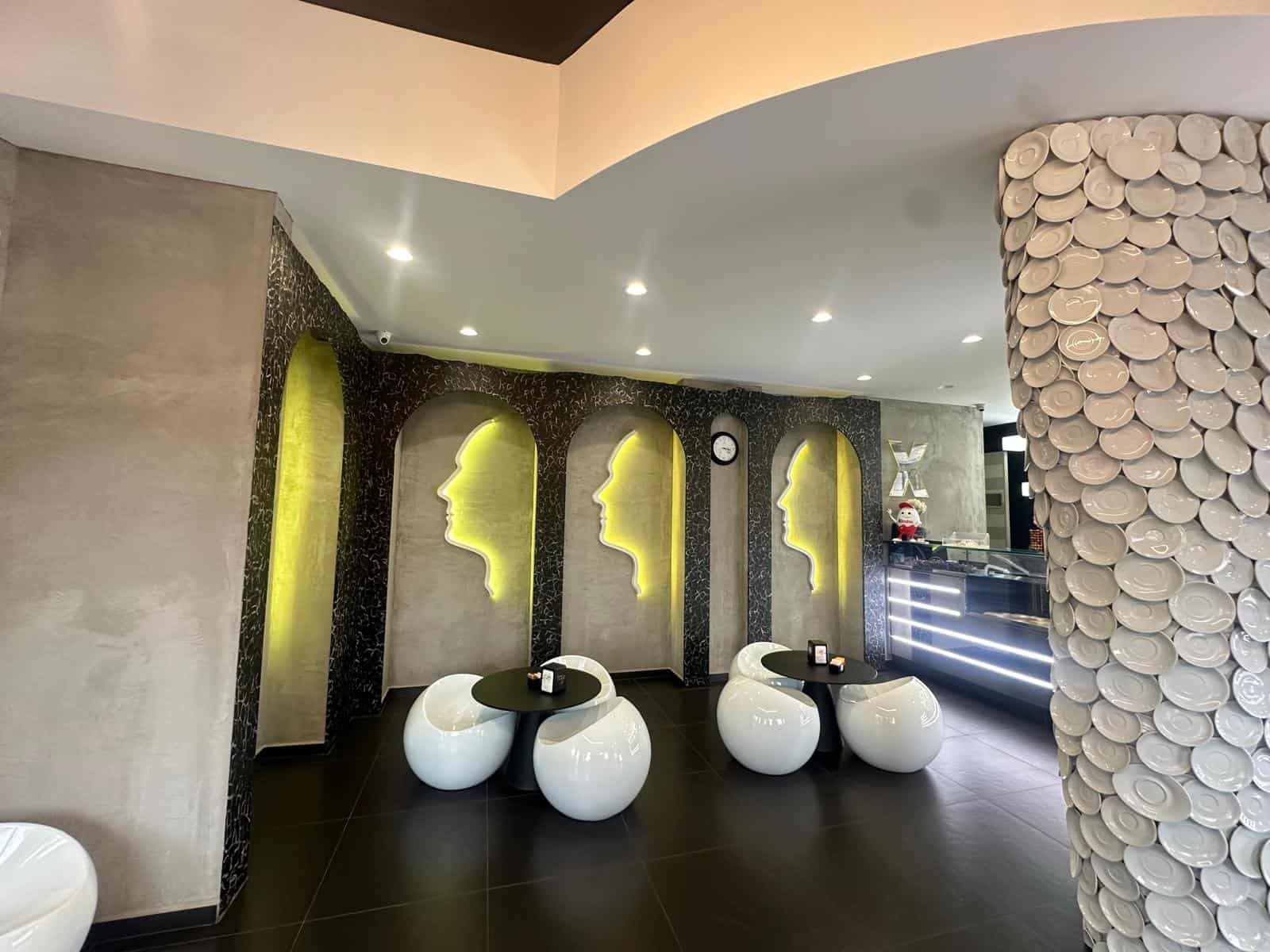 Elegante zona di accoglienza moderna con pareti a firma stilizzata illuminata e arredi contemporanei, ideale per ambienti di lavoro o locali di design raffinato.