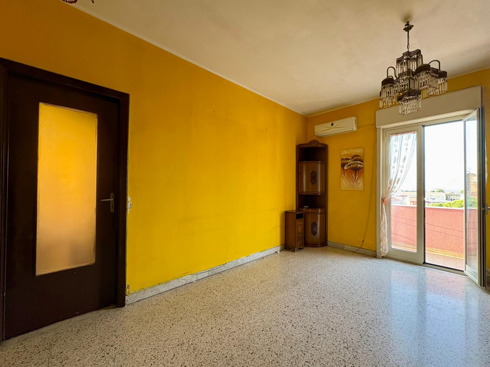 Spazioso soggiorno luminoso con pareti gialle e accesso al balcone, ideale per living e relax, arredi essenziali e illuminazione centrale.