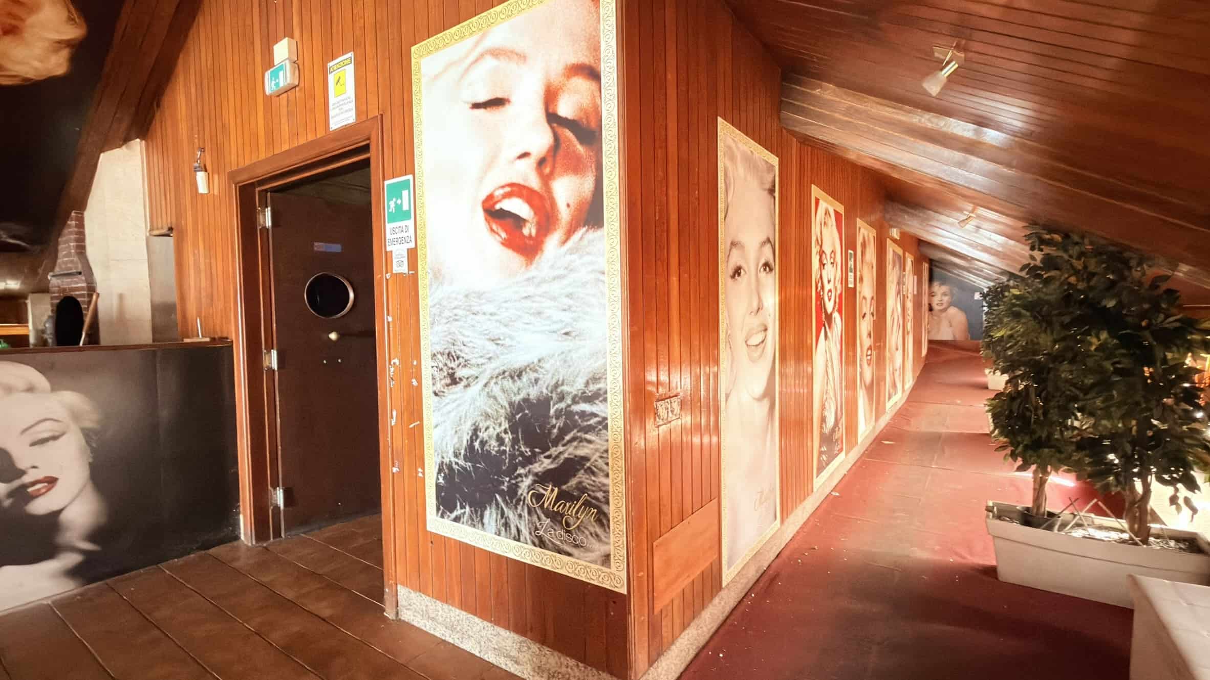 Elegante corridoio con pareti rivestite in legno, decorato con poster artistici di icone famose, ambiente raffinato e accogliente, ideale per promuovere servizi immobiliari NextCasa e occasioni di investimento.