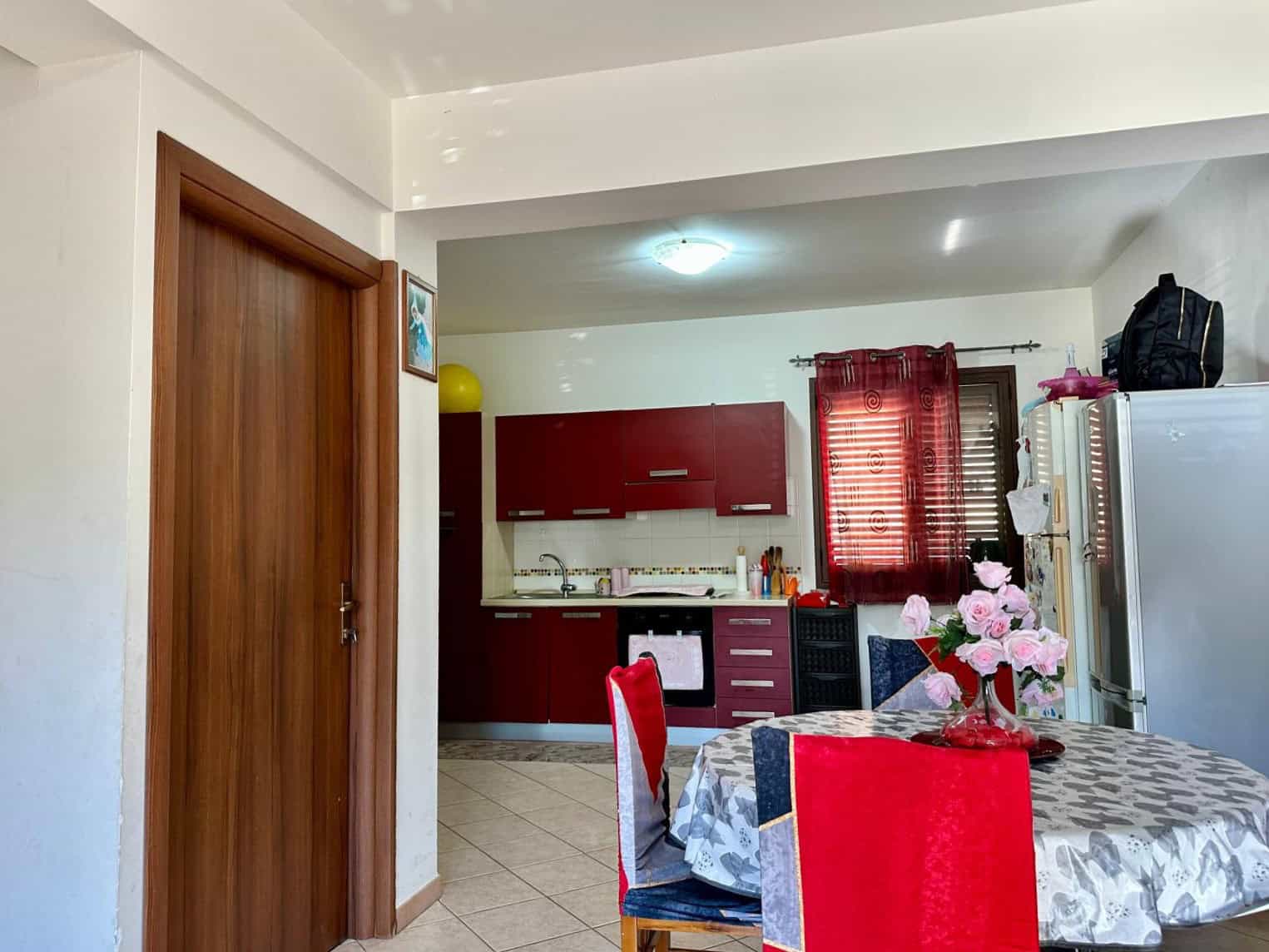 Lavagna da pranzo con fiori rosa in cucina, mobili rossi, soggiorno accogliente, arredamento pratico, casa in vendita, stile moderno, casa confortevole, soluzione abitativa, NextCasa, immobili Italia.