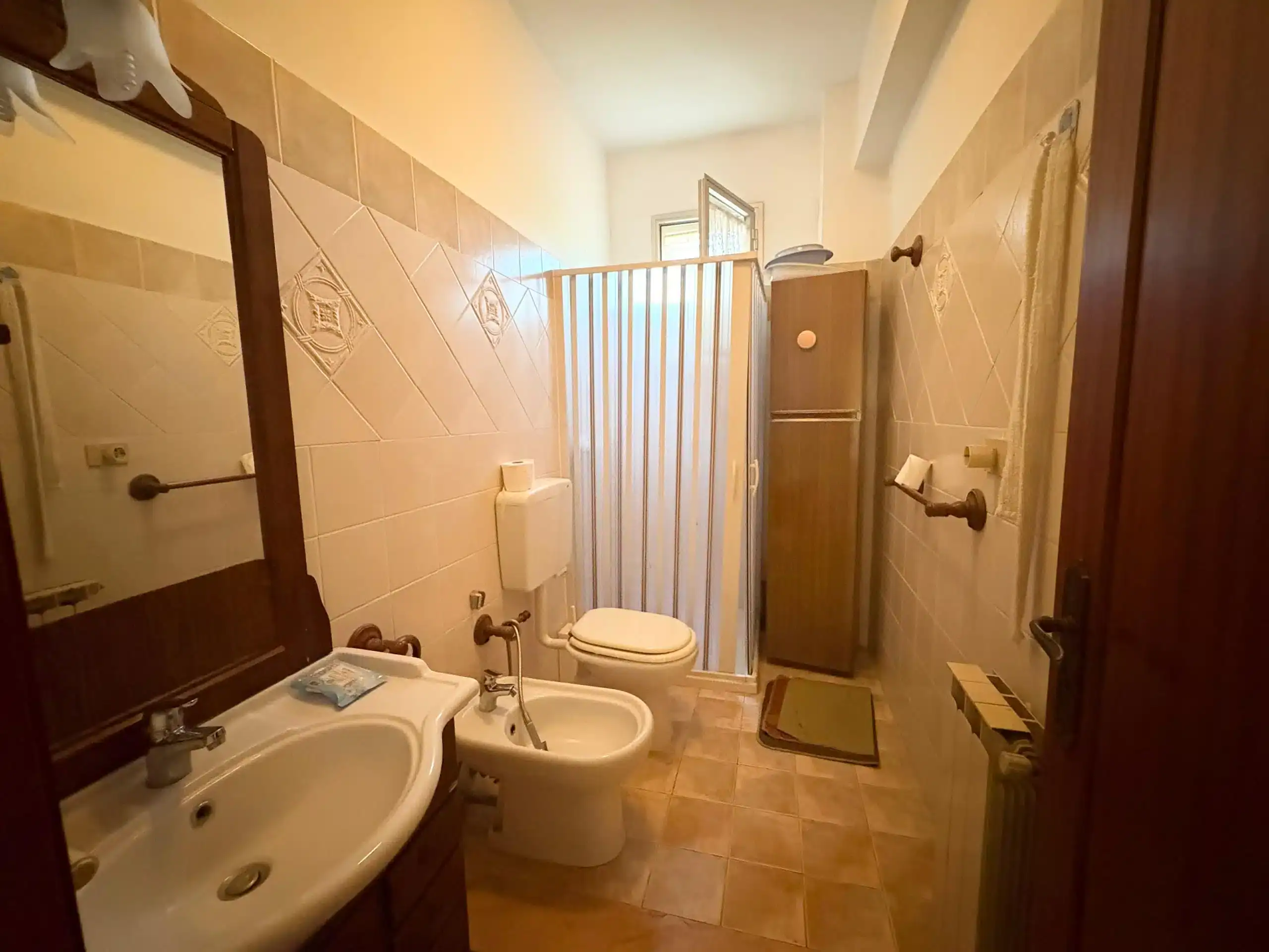 Lavabo e bagno con tenda doccia, bagno in stile classico, pareti rivestite con piastrelle beige, mobili in legno e accessori funzionali, ambiente bagno accogliente e pratico.