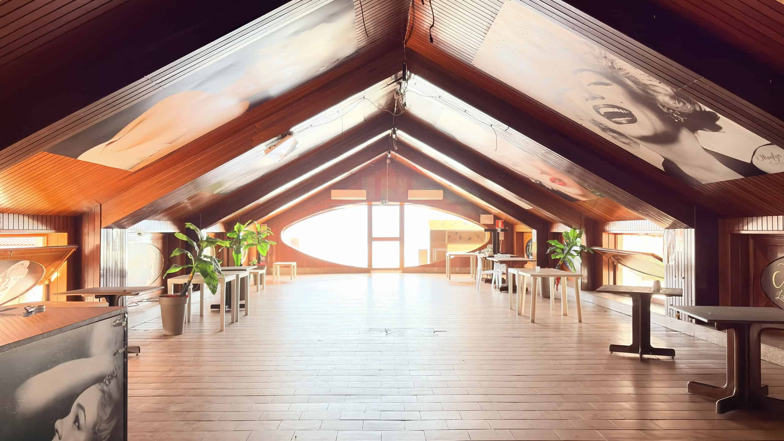 Elegante soffitta in legno con pareti e soffitto decorati con poster di Marilyn Monroe e musica, luminoso ambiente con grandi finestre, ideale per eventi e feste private.