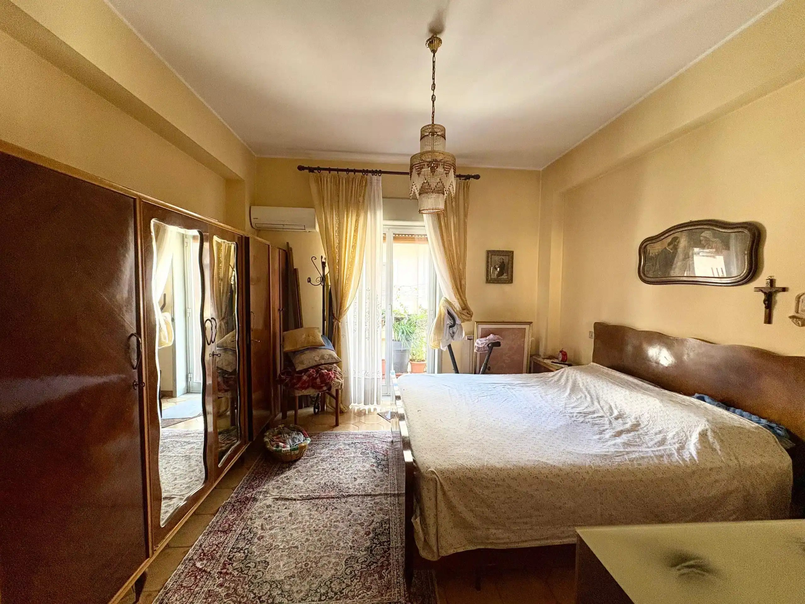 Movimento di luce naturale in camera da letto con mobili classici, armadio antico e balcone soleggiato, ideale per appartamenti in affitto o vendita a NextCasa.