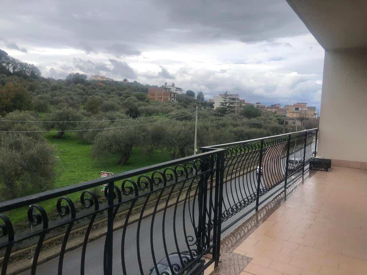 Vista panoramica da balcone con grate in ferro battuto, campagna verdeggiante e case moderne, atmosfera tranquilla e naturale, ideale per residenze a NextCasa.