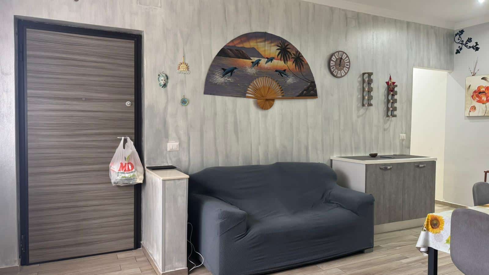 Angolo soggiorno con pareti decorate, divano, arte murale e accessori in stile tropicale in ambiente casa NextCasa.