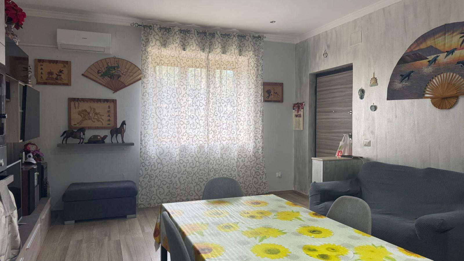 Appartamento arredato con stile tradizionale, soggiorno accogliente con decorazioni d'ispirazione asiatica, tende leggere e divano spazioso, ideale per affitti turistici o residenziali.