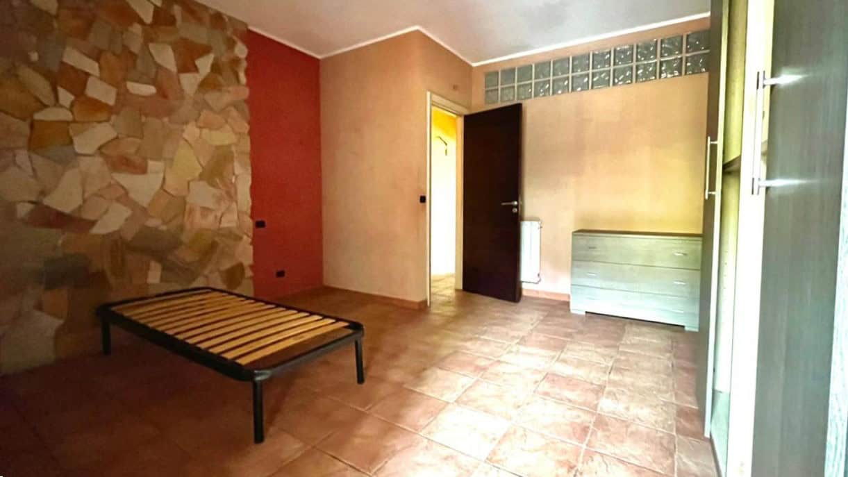 Arredo camera da letto minimalista con pareti colorate e pavimento in piastrelle, presente armadio e cassettiera in stile moderno, spazio versatile e funzionale.