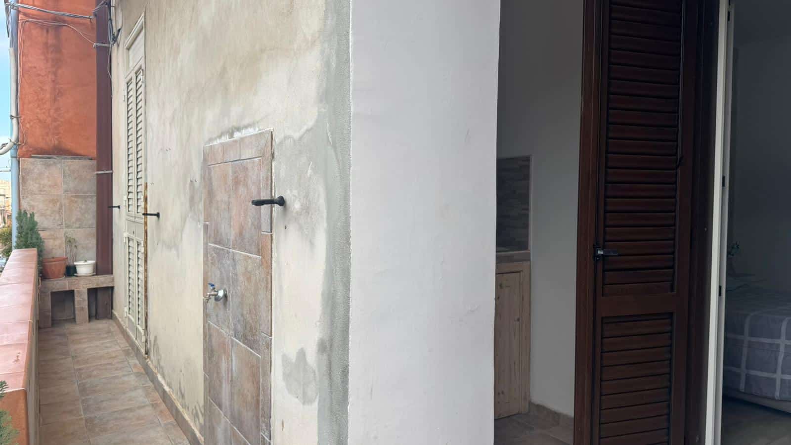1. Spazio esterno con pareti in pietra e terrazza, ideale come balcone o area relax, con accesso a interni con porte scorrevoli in legno.