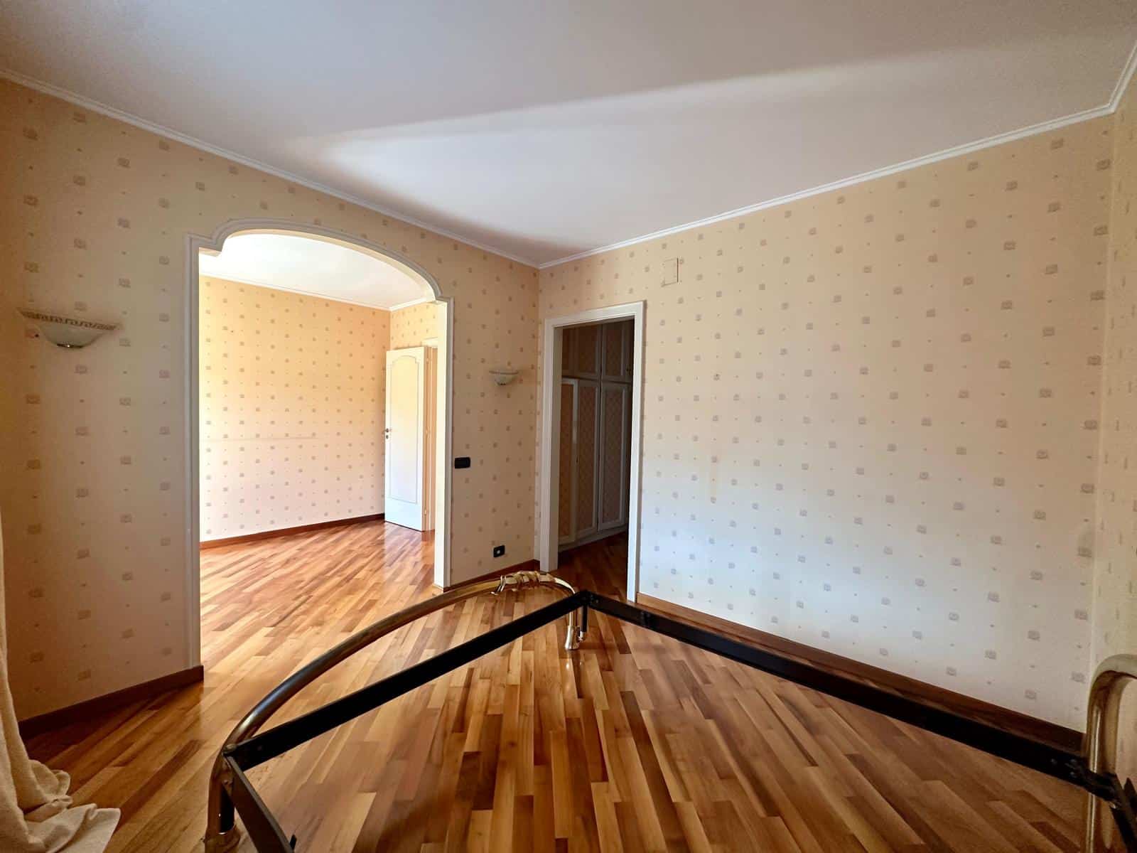 Ampio soggiorno elegante con pareti color crema, pavimento in parquet, illuminazione soffusa e accesso alle camere adiacenti, ideale per ambienti di vivere confortevoli e luminosi.