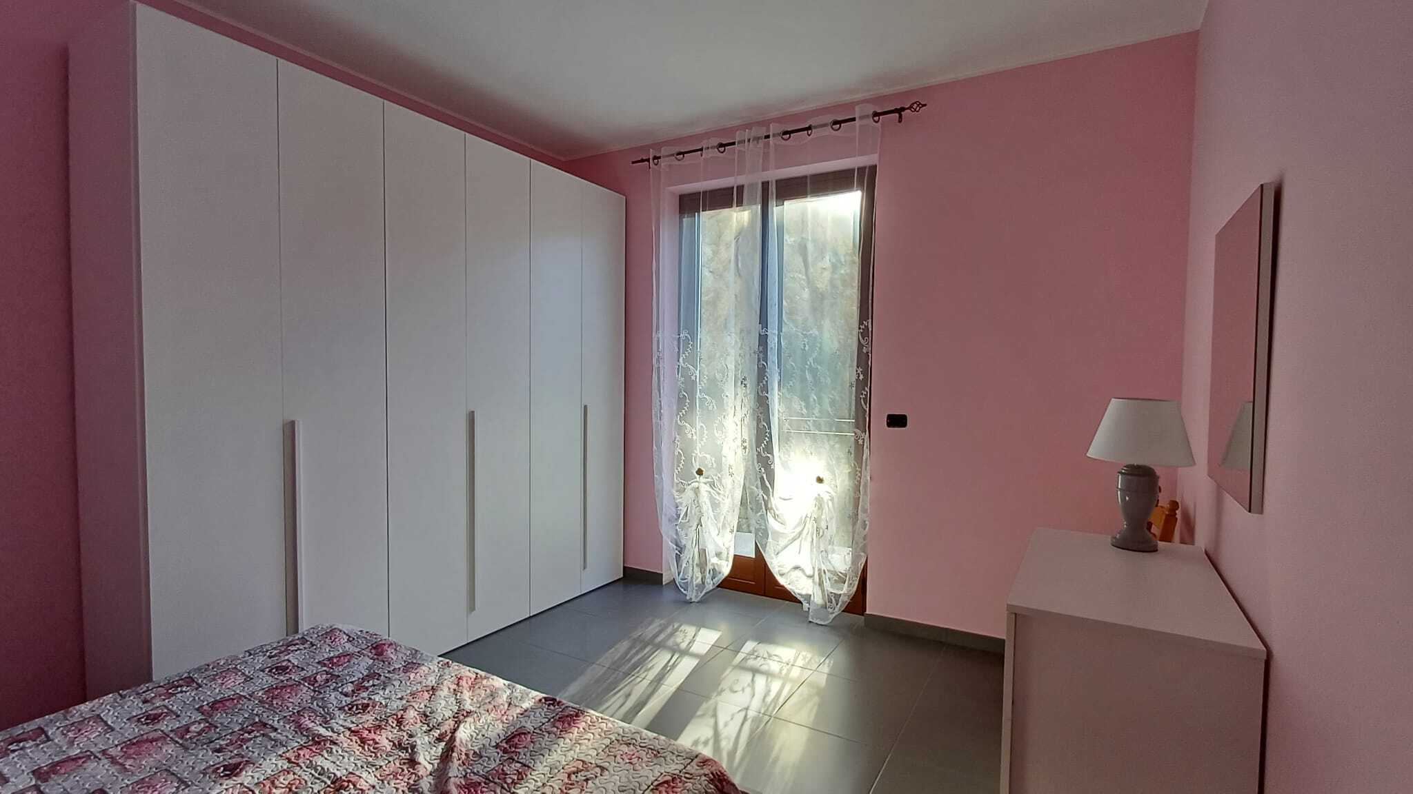 1. Armadio a muro bianco in camera con pareti rosa e finestra con tendina trasparente.