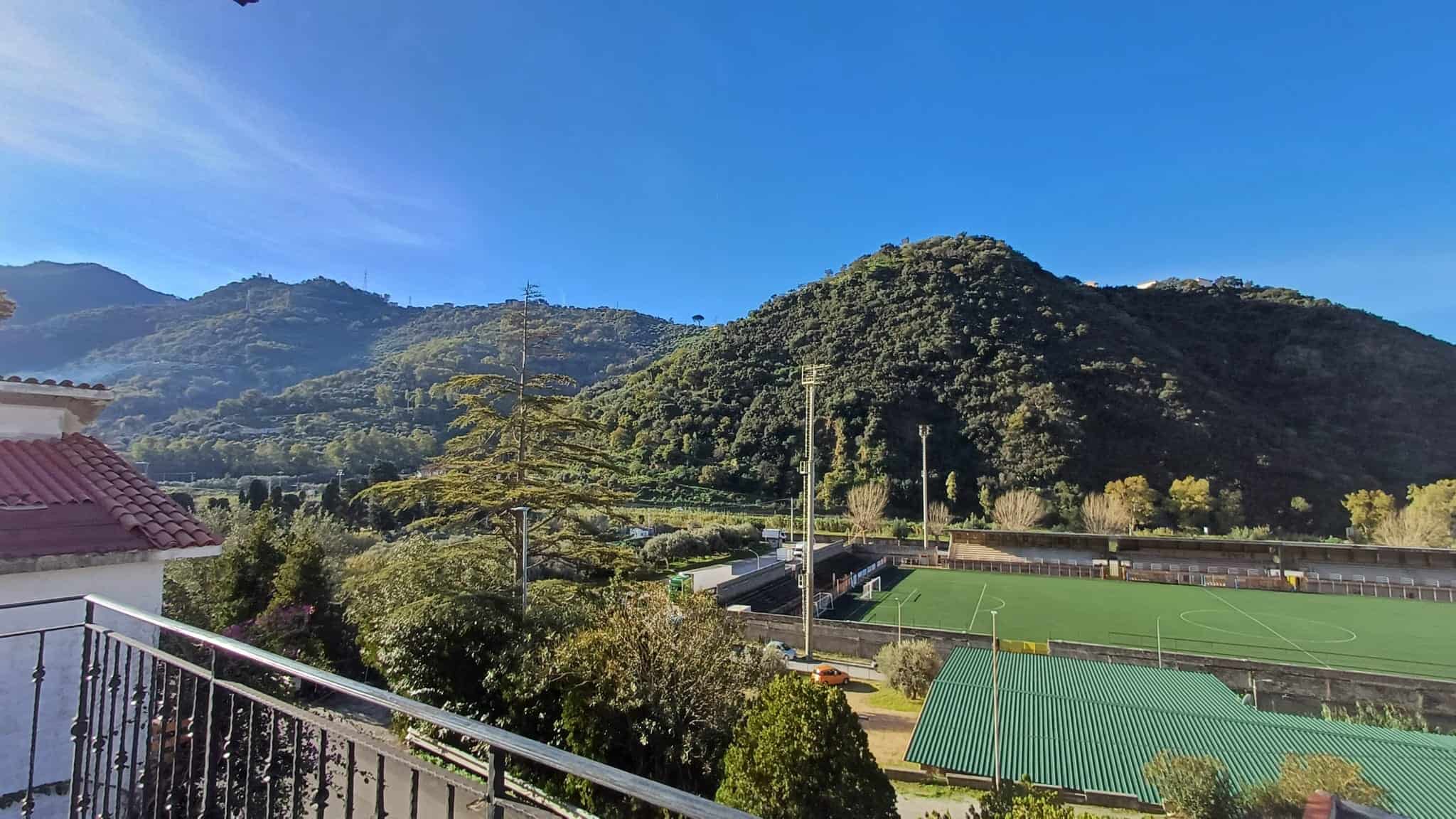 1. Vista panoramica delle montagne e del campo da calcio in un paesaggio naturale con cielo azzurro e vegetazione rigogliosa.
