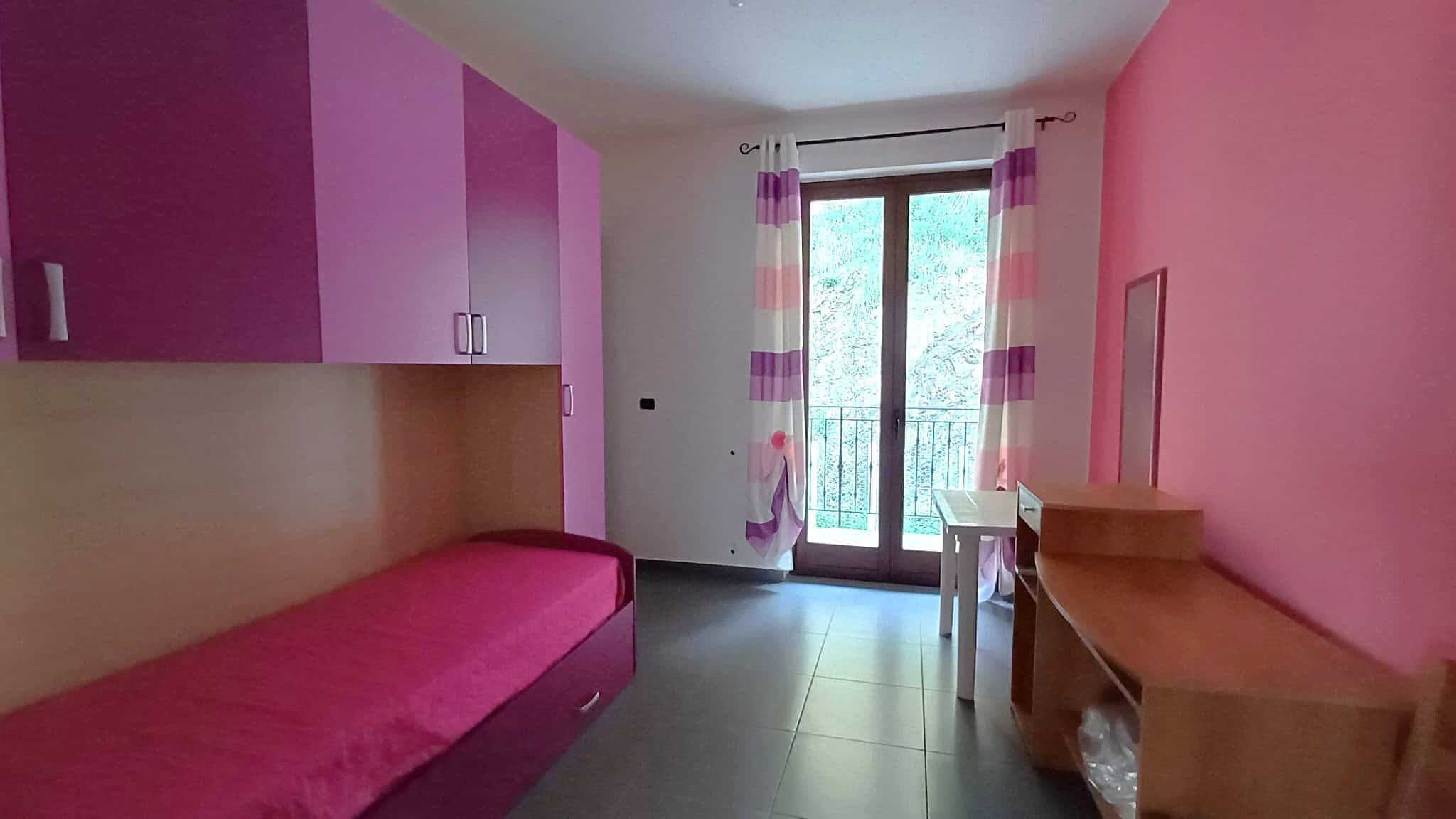 Letto singolo in stanza con mobili colorati e vista su balcone, ideale come soluzione di arredamento per case e appartamenti in vendita o affitto, in zona residenziale.