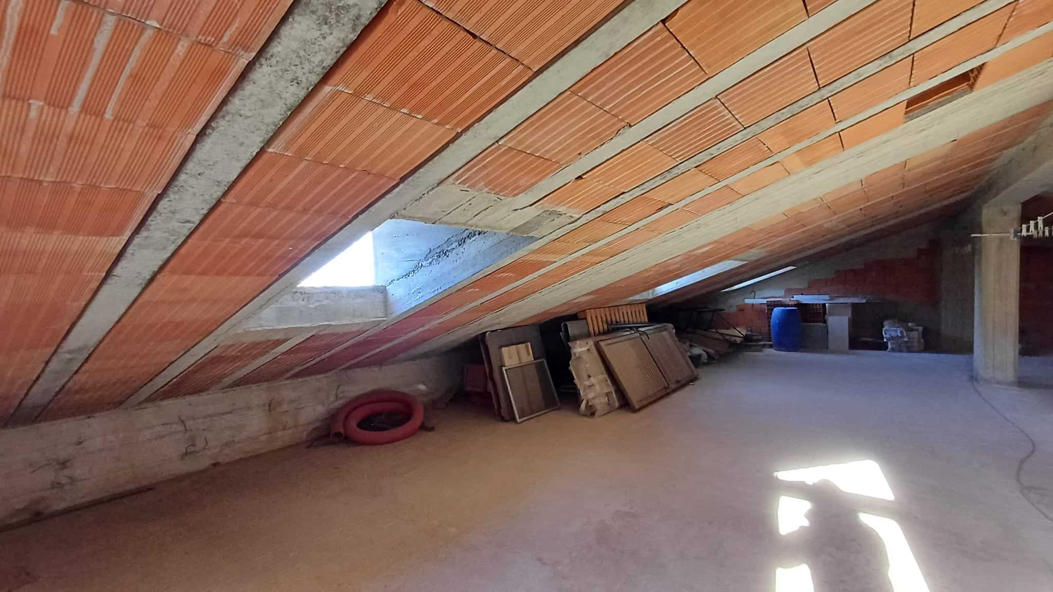 Facciata interna in costruzione, con pareti in mattoni e soffitto inclinato in fase di finitura, spazio ideale per ristrutturazioni e lavori di isolamento termico.