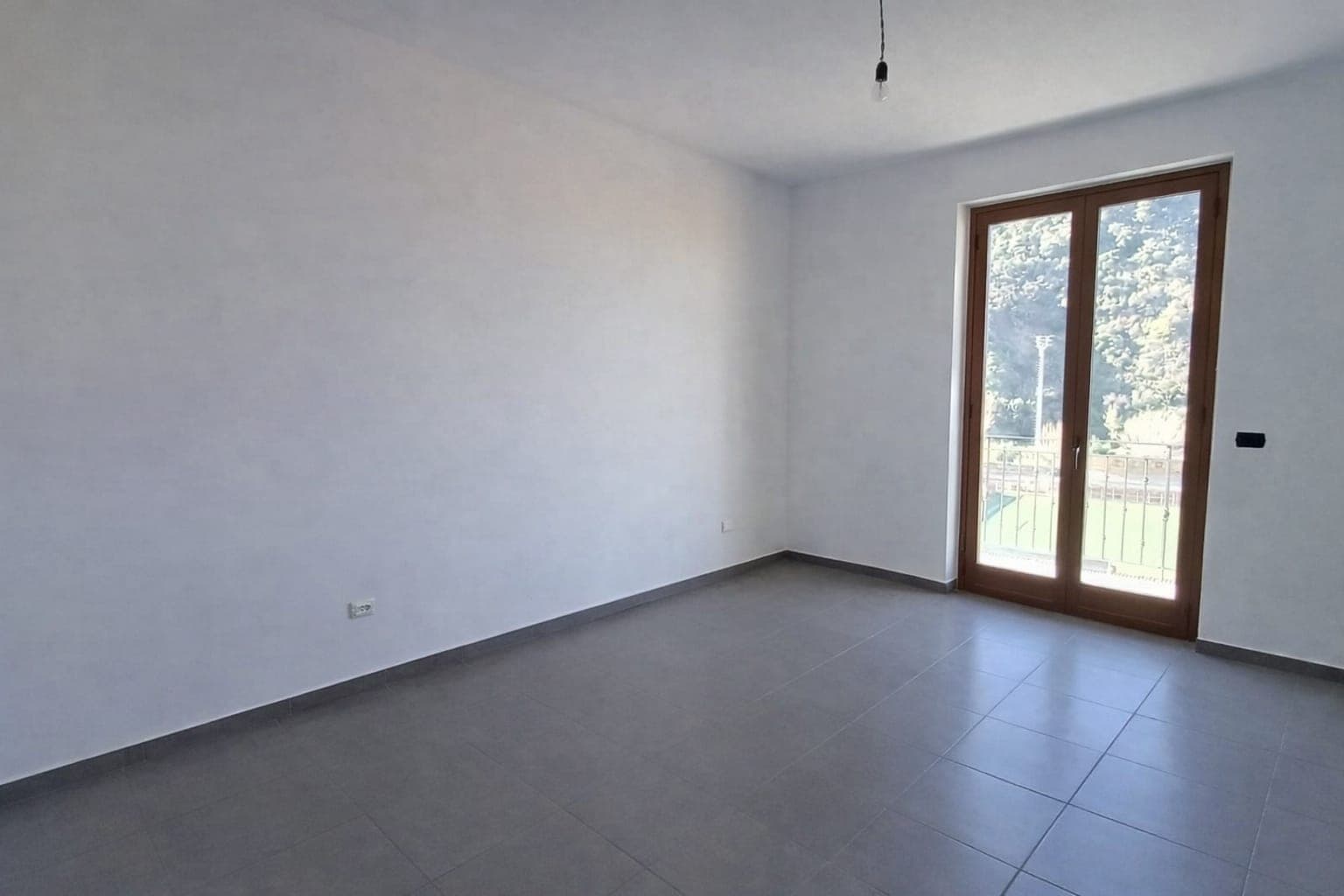 Spazio luminoso con grande porta finestra e vista sul verde, ideale per soggiorno o camera da letto, con finiture moderne e pavimento in gres porcellanato ad alta qualità.