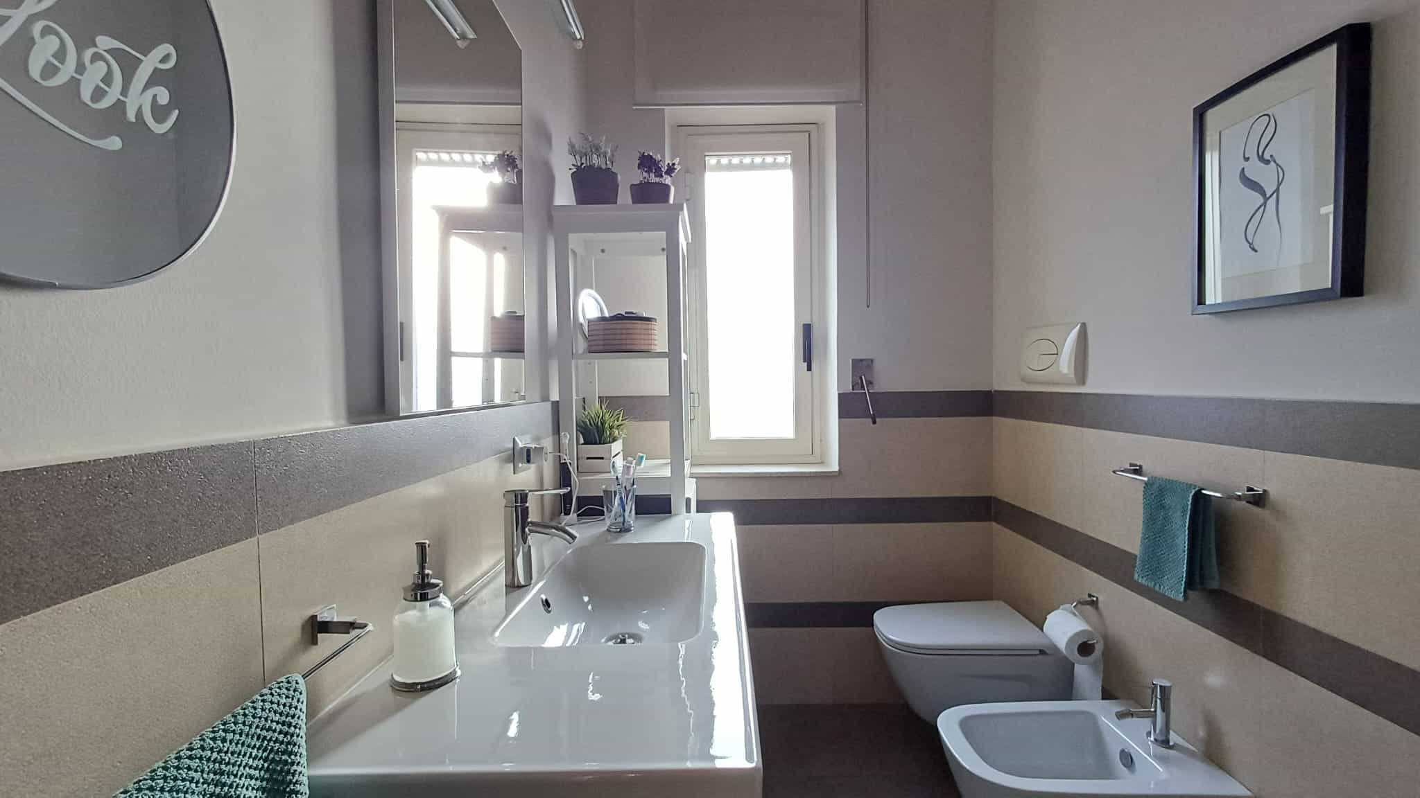Lavabo e bidet moderni in bagno con arredamento funzionale e decorazioni di stile, illuminato da luce naturale, ideale per servizi di case e appartamenti in vendita o in affitto.