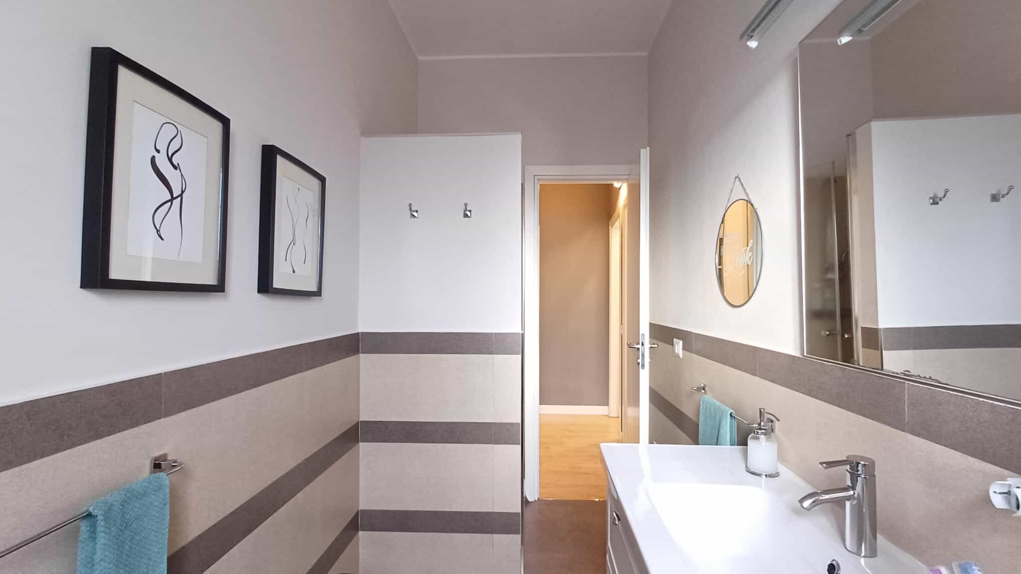 Immagine di un moderno bagno con rivestimenti beige e grigi, lavabo elegante e ampia superficie specchiera, decorato con quadri astratti e specchio rotondo, ideale per case e appartamenti di design.