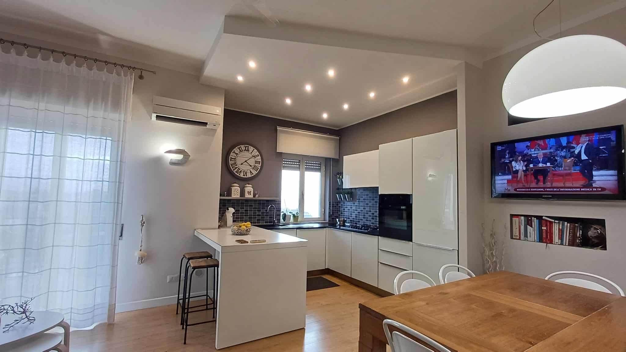 1. Cucina moderna con mobili bianchi, openspace luminoso e pareti grigie, dettagli di design, elettrodomestici integrati, e tavolo in legno, ideale per appartamenti di lusso.