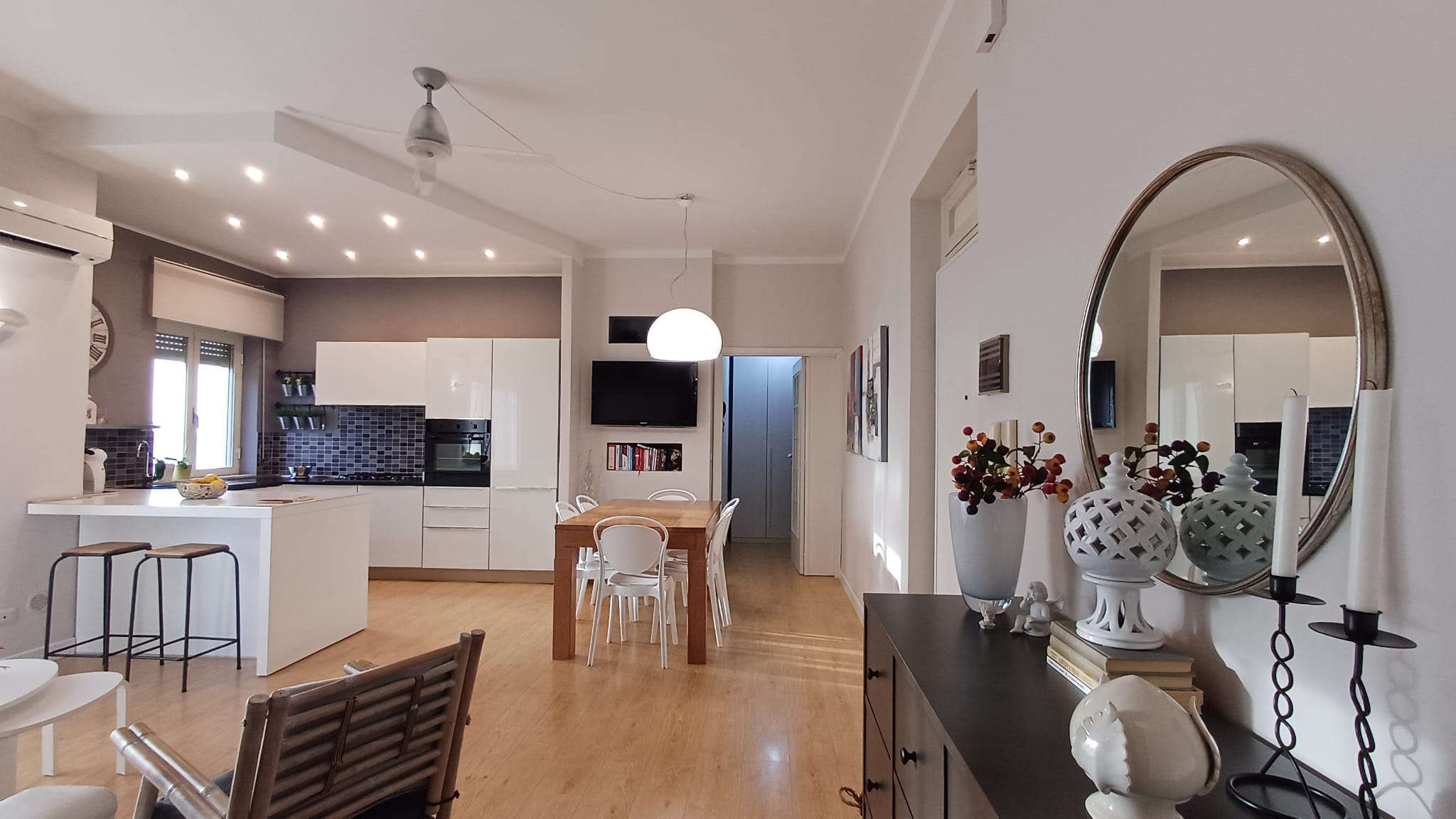 Spazi abitativi moderni e luminosi con cucina a parete bianca, zona pranzo in legno e dettagli decorativi eleganti in bianco e nero, ideali per case di prestigio.