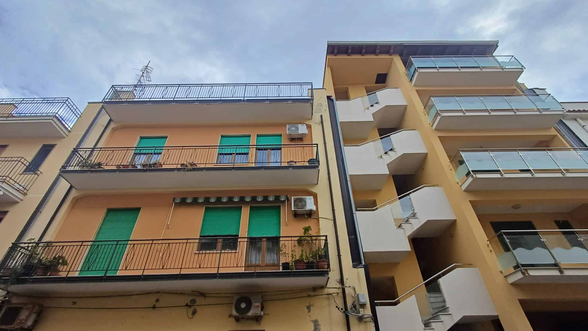 Balconi di appartamenti residenziali con facciata moderna e balconi con ringhiere in metallo, in un edificio urbano con ampie finestre e aria condizionata, sotto un cielo nuvoloso.