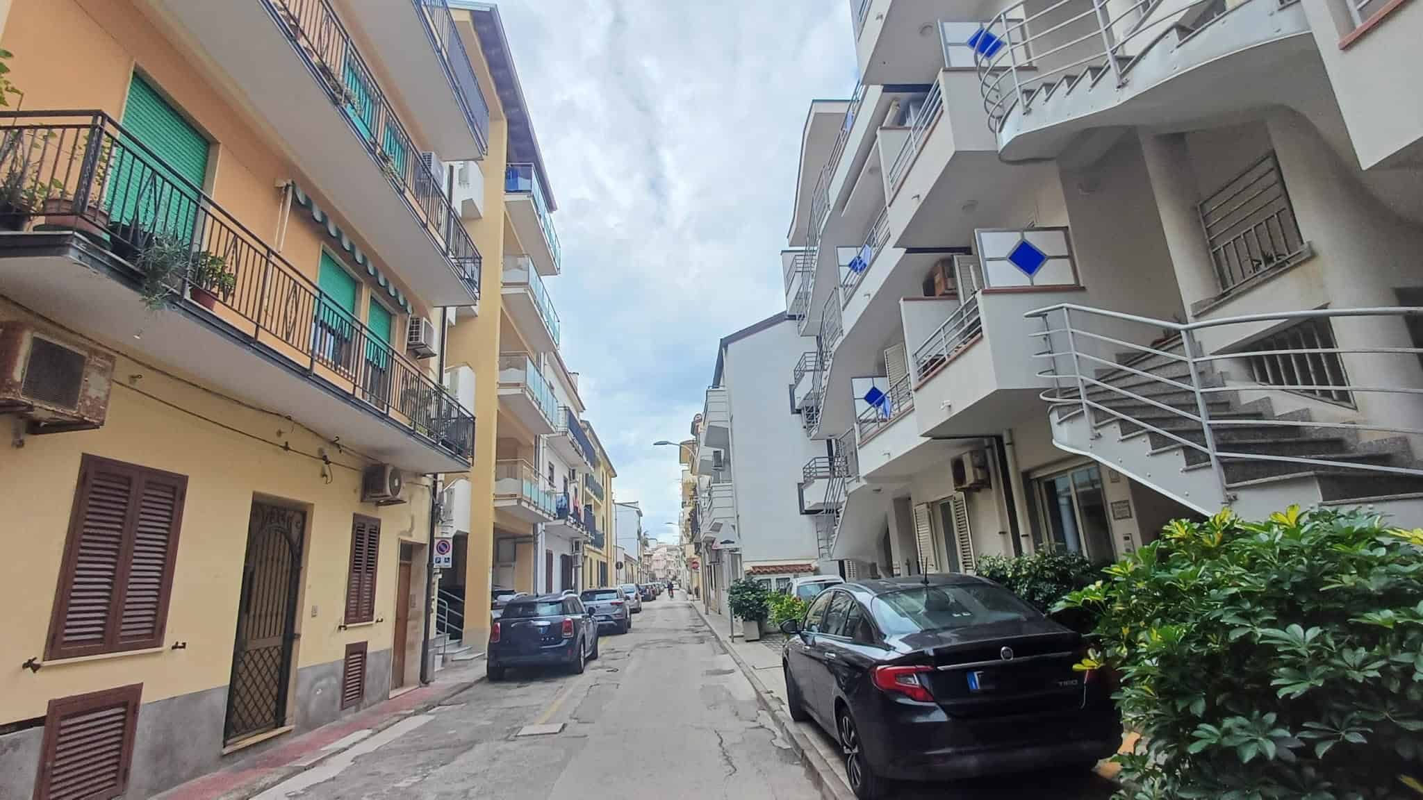 Strada urbana con edifici residenziali e auto parcheggiate, vista di un quartiere residenziale in Italia con edifici moderni e balconi.