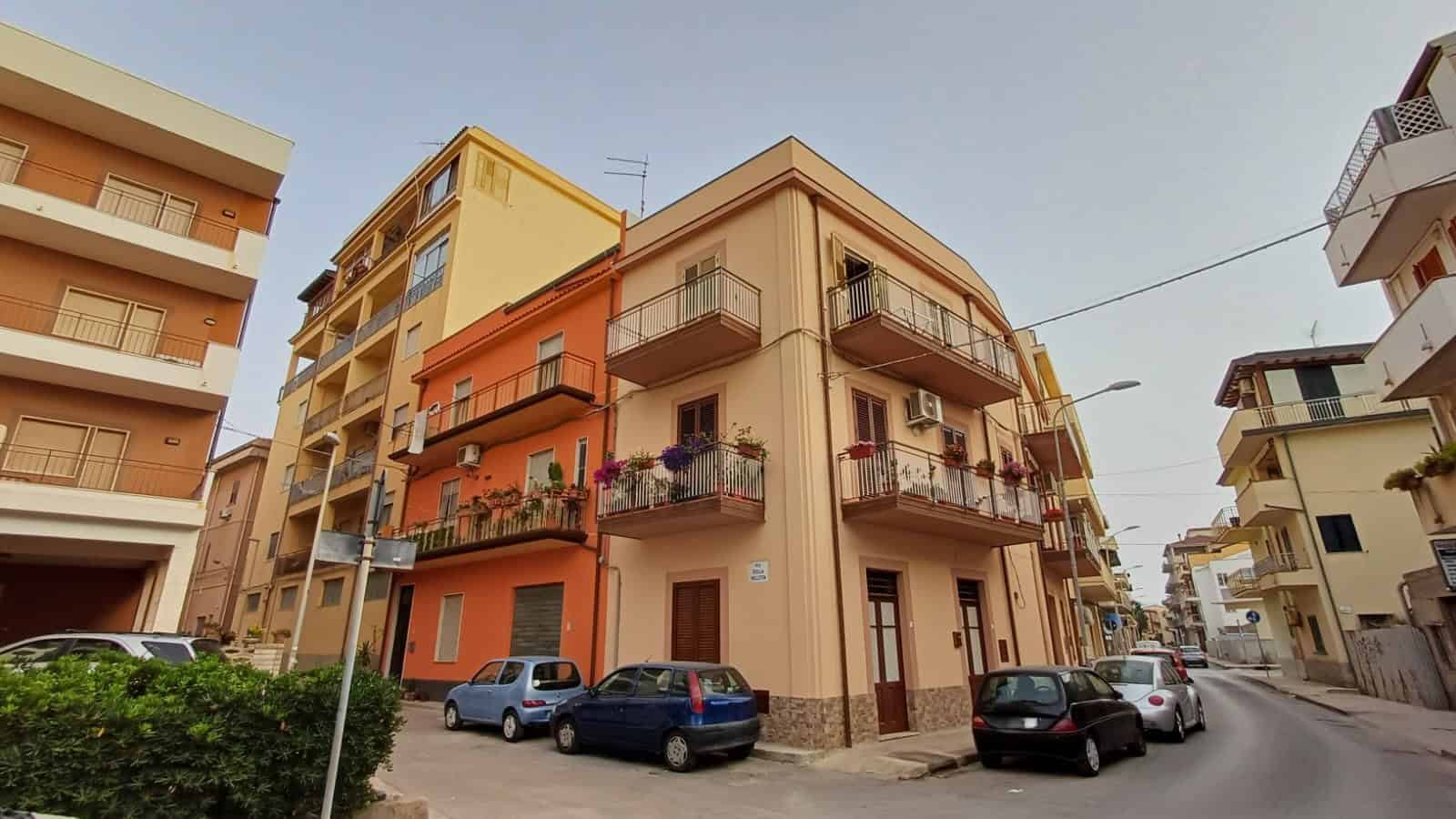 Ampio edificio residenziale in stile Mediterraneo con balconi fioriti, parcheggio e ambienti accoglienti, situato in zona tranquilla ideale per vivere e investire nel mercato immobiliare.
