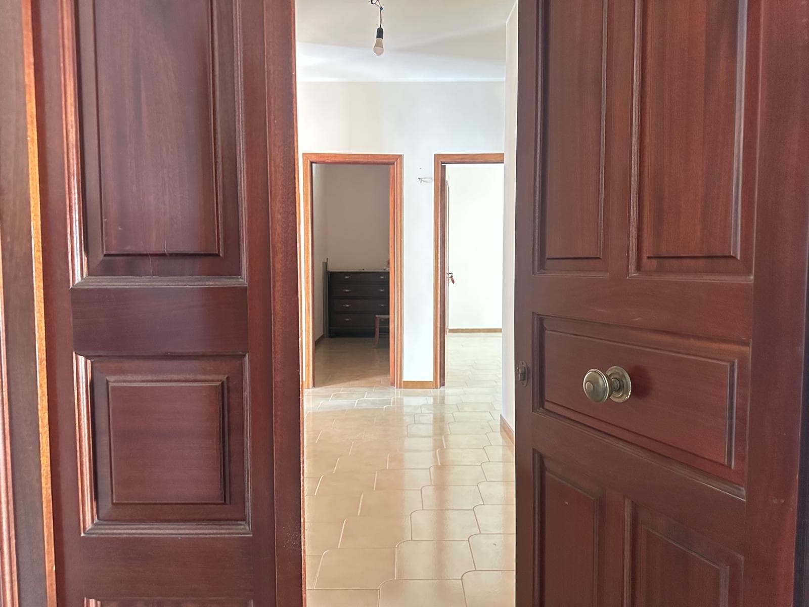 Esterna di un appartamento con porte in legno massello, ingresso illuminato e pavimento in ceramica beige. Vista di stanze interne con infissi in legno e ambiente luminoso.