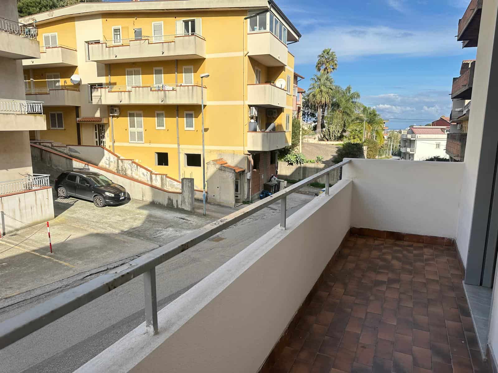 Vista panoramica dal balcone di un appartamento con pavimento in piastrelle e ringhiera in metallo, vista su edifici residenziali e palmizi, ideale per investimento immobiliare NextCasa.