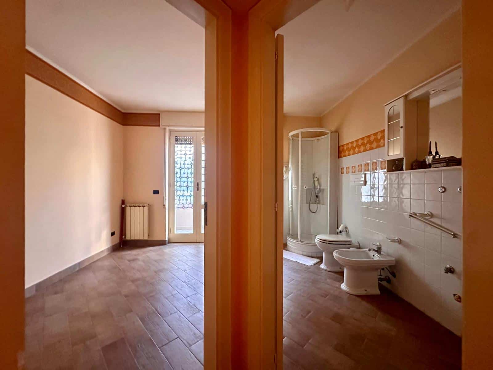 Appartamento con soggiorno luminoso e balcone, bagno con doccia, bidet e WC in stile classico, pavimenti in gres effetto legno, ideale per investimento o prima casa.