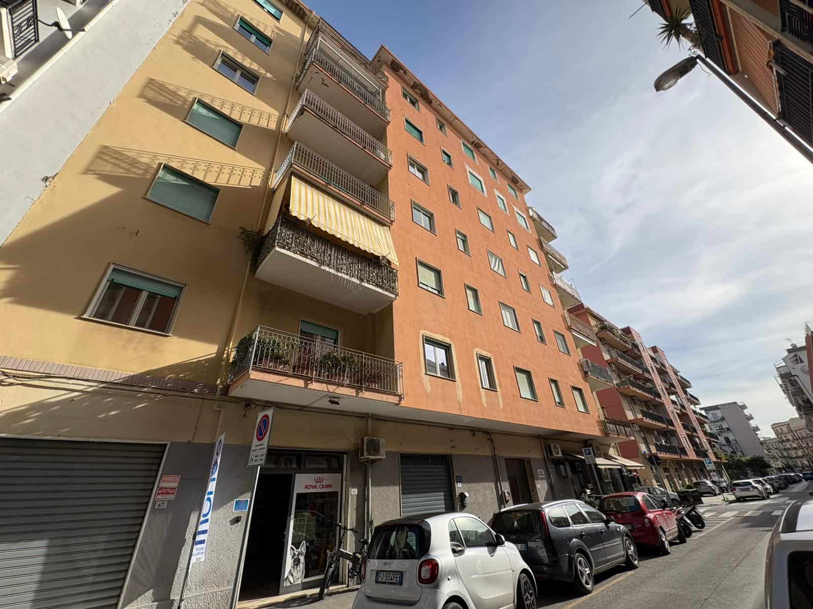 Edificio residenziale alto in centro città con balconi e facciata colorata, in zona urbana con parcheggio e attività commerciali, ideale per trovare casa moderna e funzionale.