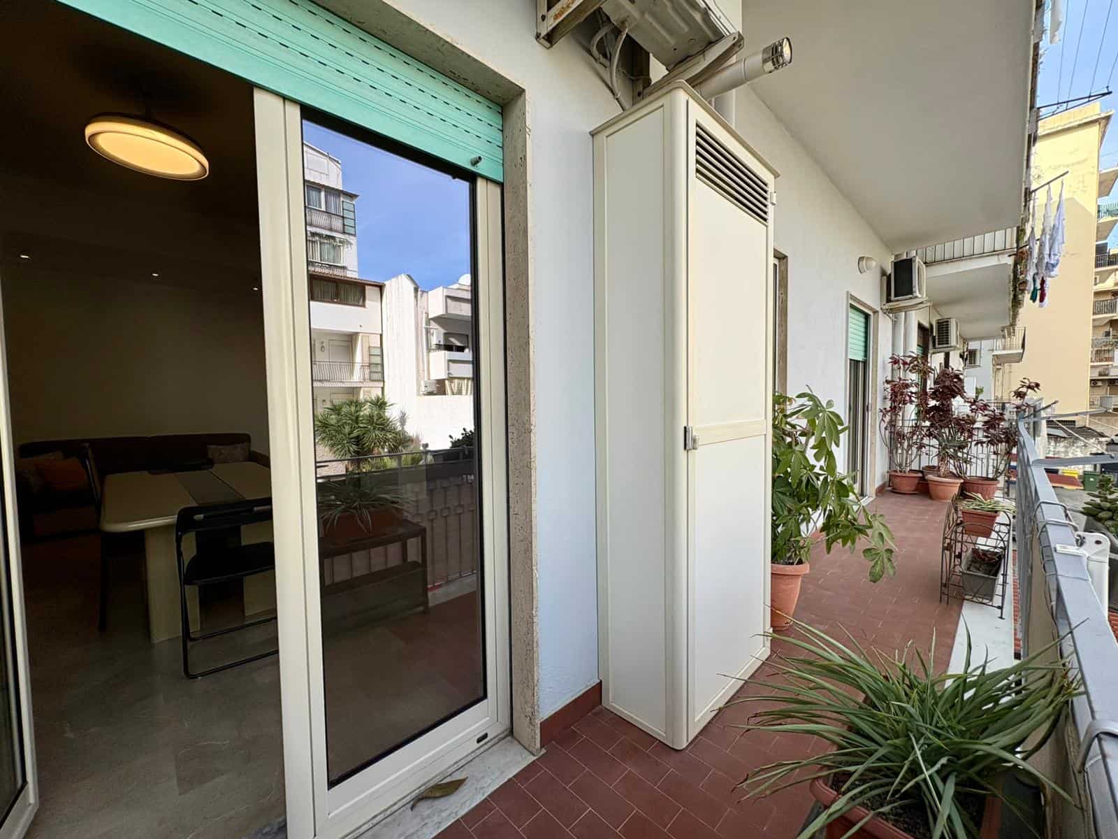 Balcone di appartamento con piante, vista città, e accesso a soggiorno con grande finestra e arredamento minimal. Ottima soluzione per vivere all'aperto vicino al centro urbano.