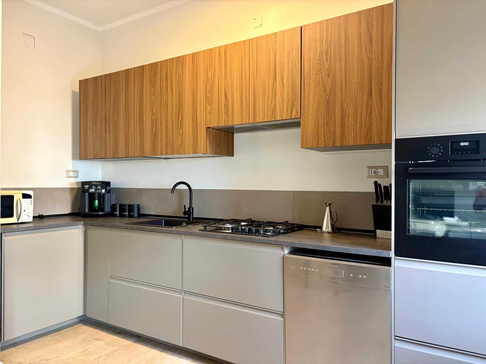 Cucina moderna con ante in legno e piano in gres, elettrodomestici integrati, piano cottura a gas, lavello e lavastoviglie in ambientazione elegante e funzionale.