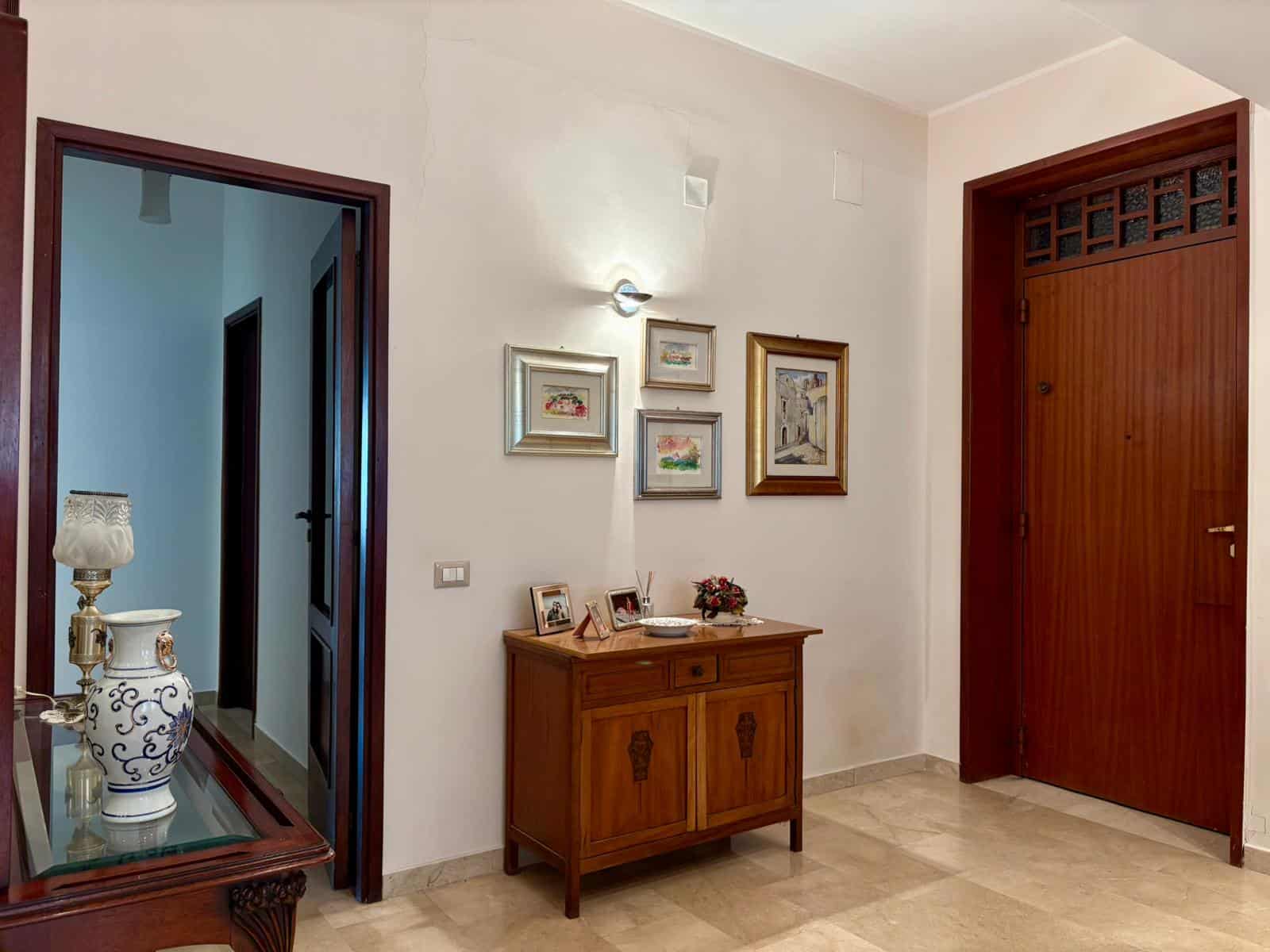 Ingresso di casa con mobili in stile classico, decorazioni floreali e pareti bianche, ideale per una soluzione abitativa elegante e accogliente - NextCasa Italia.