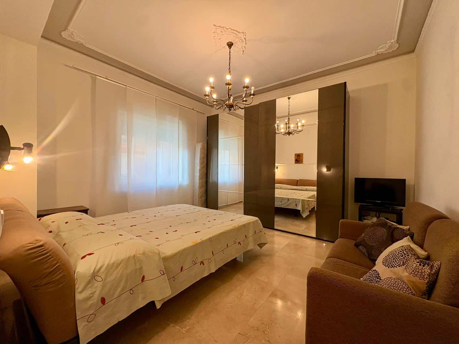 Spazio living e camera da letto in appartamento elegante con arredi moderni, letto matrimoniale, divano e televisore, illuminazione calda e dettagli di design, perfetto per affitti brevi e soggiorni di comfort.