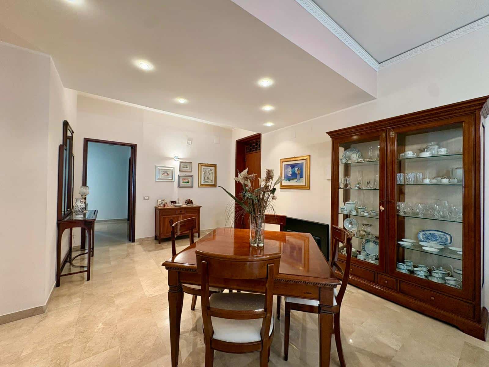 Elegante soggiorno con mobili in legno, vetrina con porcellane, tavolo da pranzo e decorazioni artistiche in stile classico e raffinato.