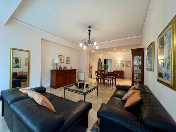 Elegante soggiorno con divani in pelle nera, arredi classici in legno, sala da pranzo e decorazioni raffinate, ideale per abitazioni di prestigio e comfort abitativo.