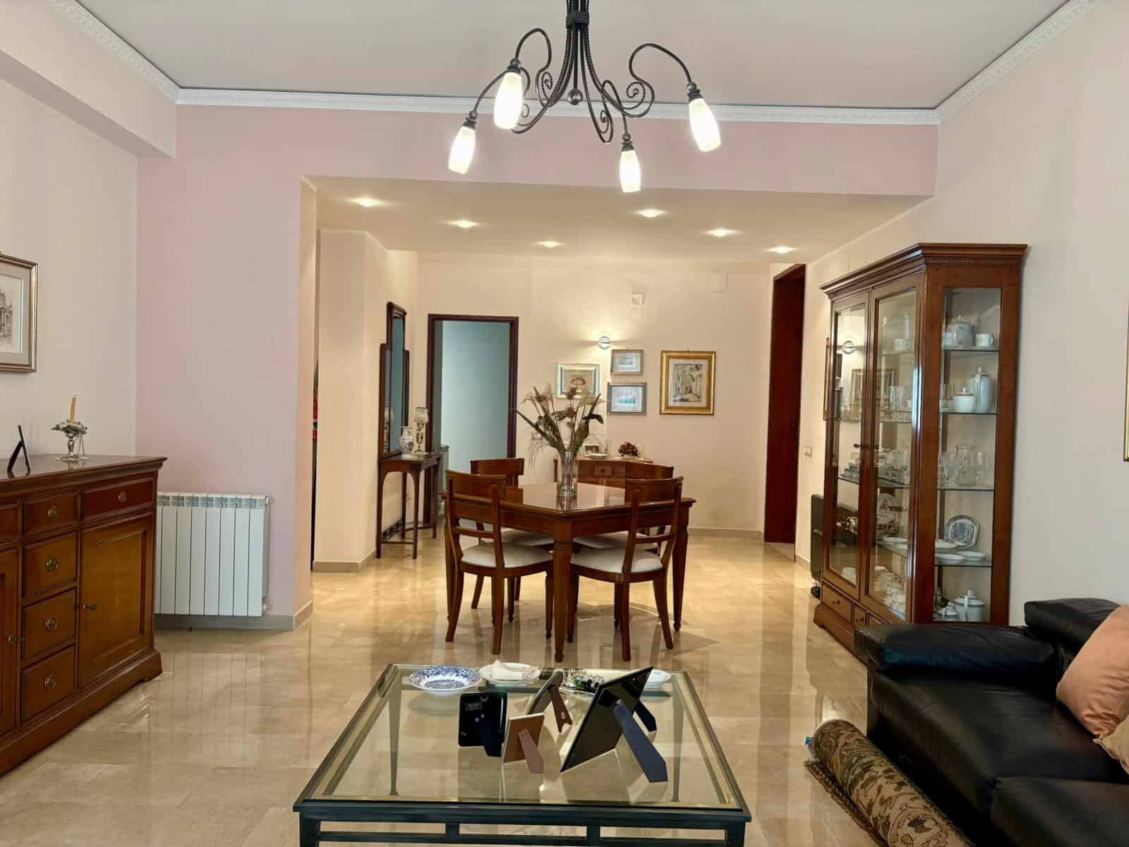 Soggiorno elegante con mobili in legno, tavolo da pranzo e vetrina, illuminazione moderna, pareti colorate, decorazioni classiche, ideale per residenze di alta qualità.