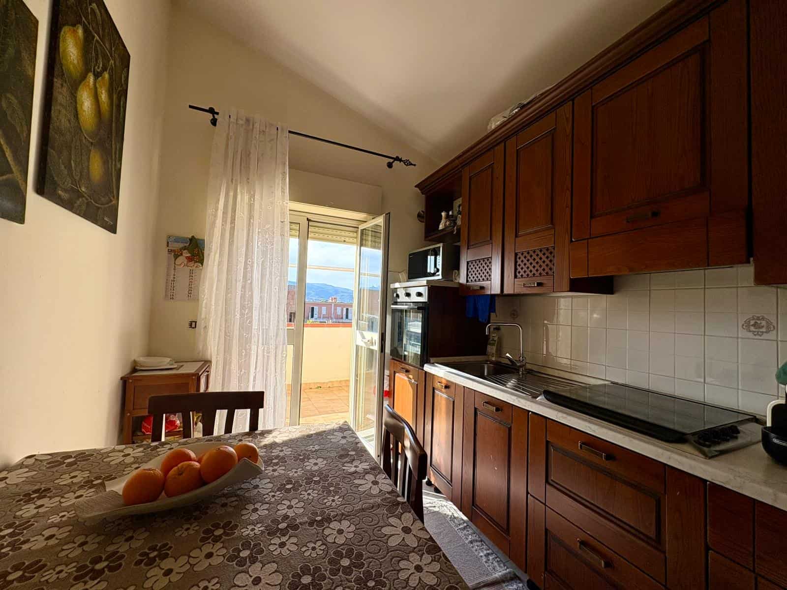 1. Cucina abitabile con armadi in legno, piano cottura elettrico e balcone con vista sulle montagne e sulla città.