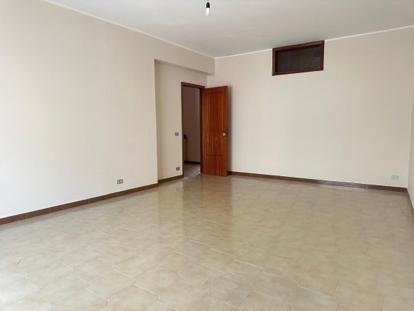 Ampio soggiorno vuoto in appartamento con pareti neutre e pavimento in ceramica, pronta per arredare e personalizzare, perfetto per migliorare i risultati di ricerca immobili di NextCasa.