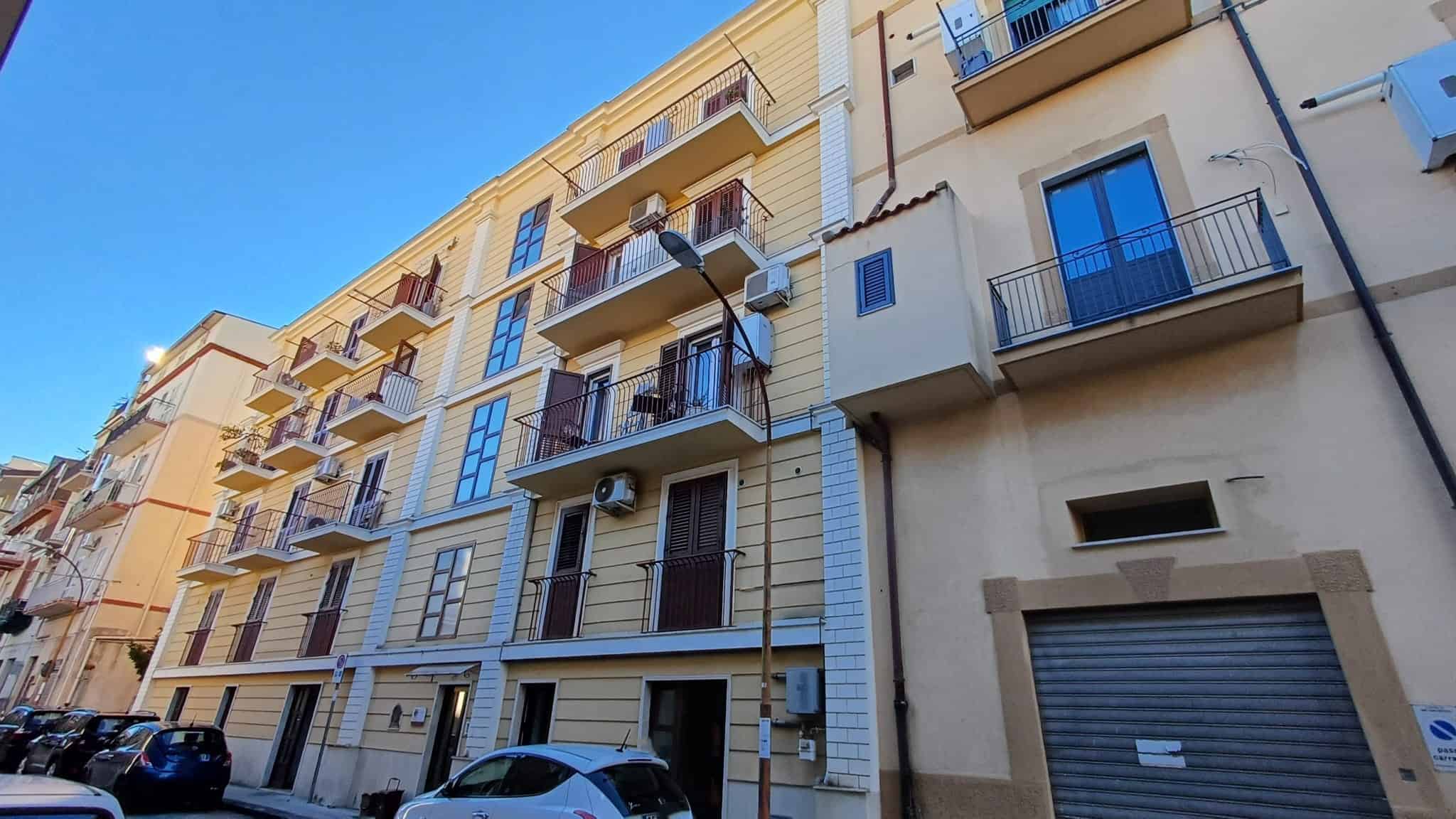 Ampio edificio residenziale con balconi e facciata moderna, situato in un'area urbana soleggiata e vivace. Ideale per chi cerca appartamenti in centro città con servizi e comfort.
