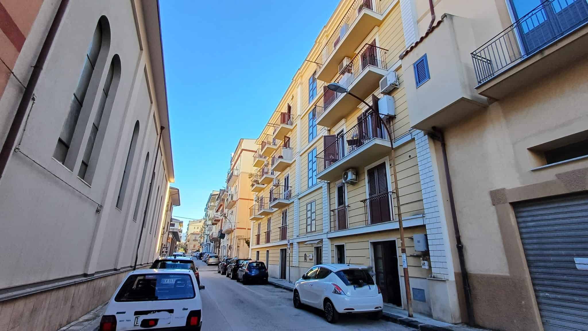 Ampio viale urbano con edifici residenziali e parcheggi, vista di giorno con cielo sereno, in zona centrale di città italiana.