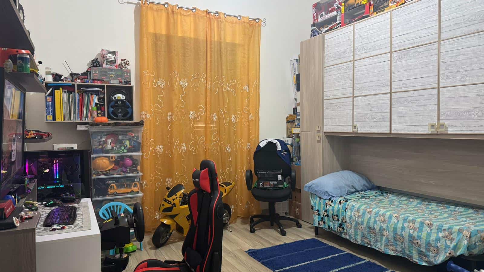 Gioco e giocattoli in camera da letto con armadio a muro e letto singolo, ambiente per bambini con scrivania, sedie gaming e decorazioni colorate per spazio creativo e divertente.