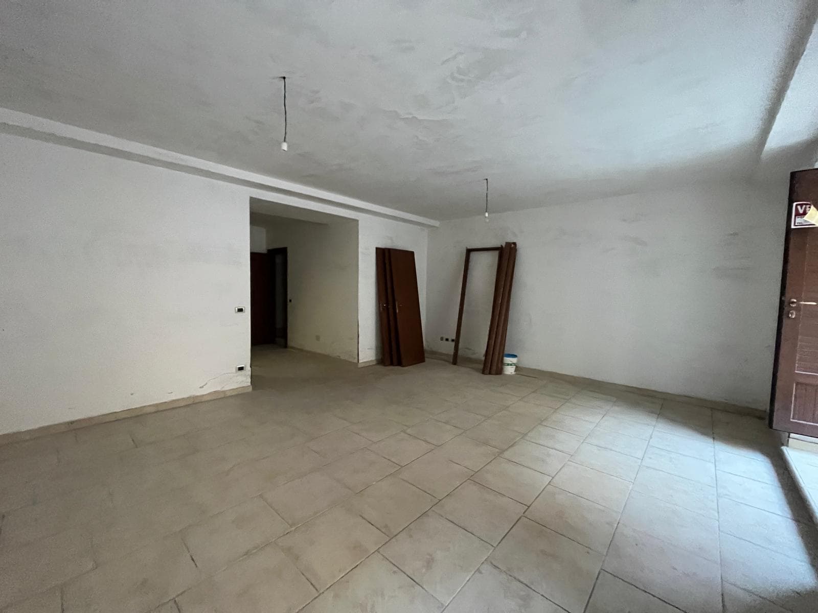 Pannello vuoto di una stanza in fase di ristrutturazione con pareti bianche e pavimento in piastrelle beige, pronta per essere arredato e personalizzato.