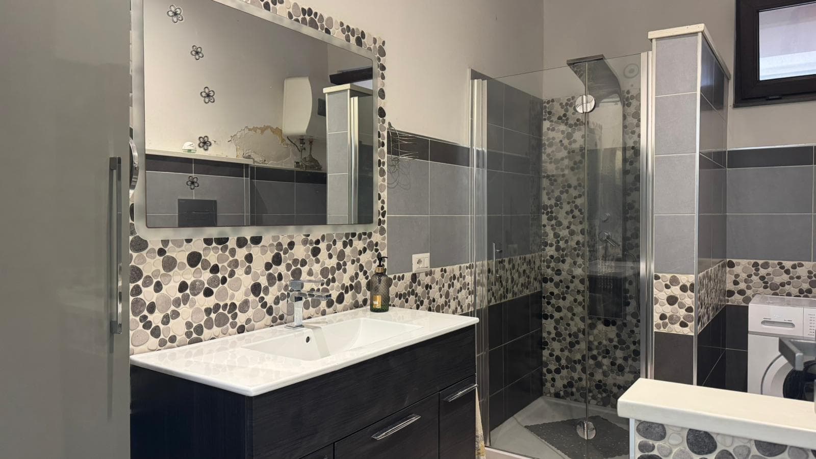 Spiegazzatura del bagno moderno con rivestimenti in piastrelle grigie e dettagli in pietra, lavabo elegante e doccia in vetro, ideale per soluzioni immobiliari di NextCasa in Italia.