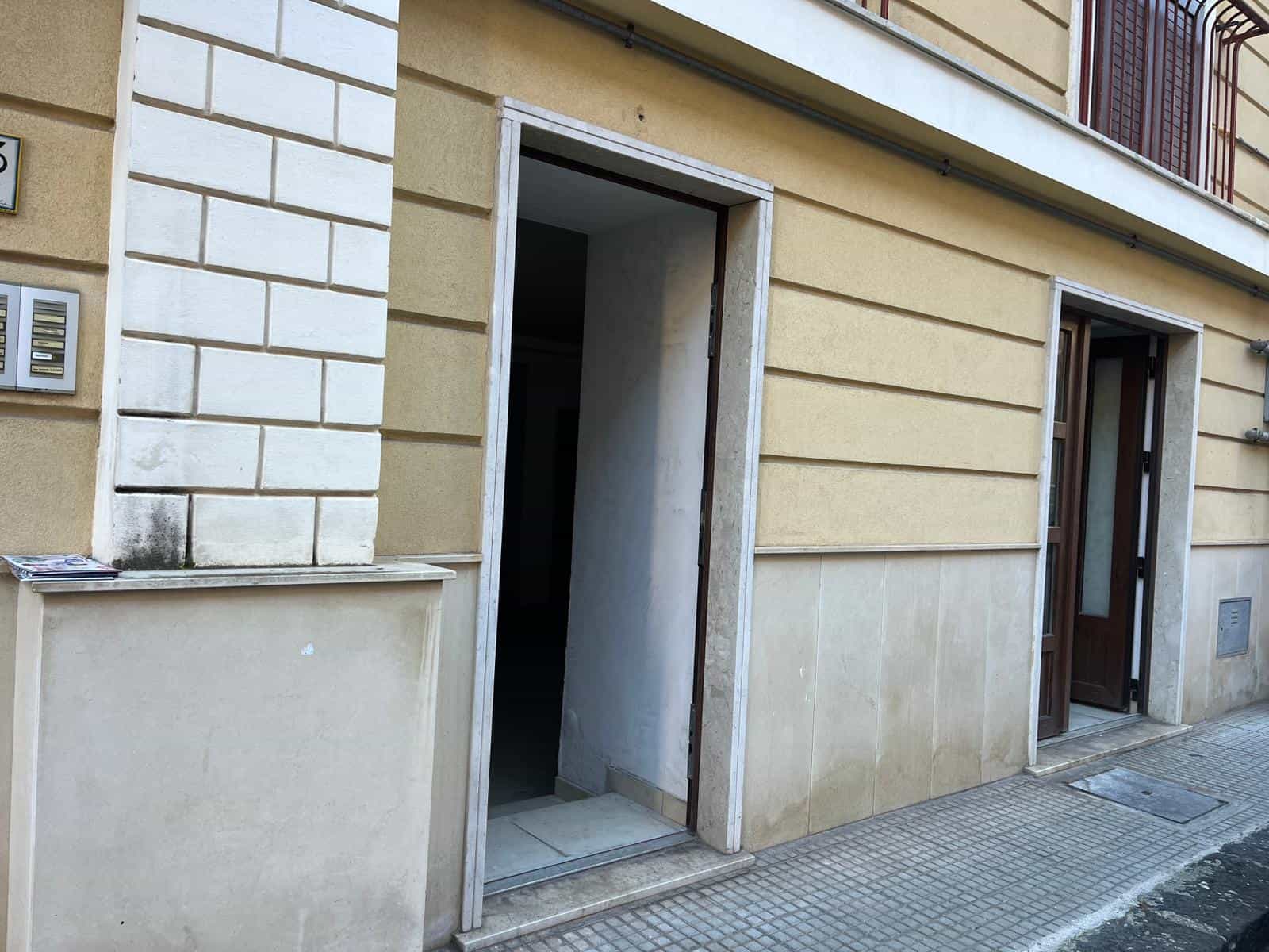 Ingresso di un appartamento in edificio residenziale con porta aperta, facciata in pietra e pareti beige, strada pavimentata in ciottolato, in stile urbano e moderno.