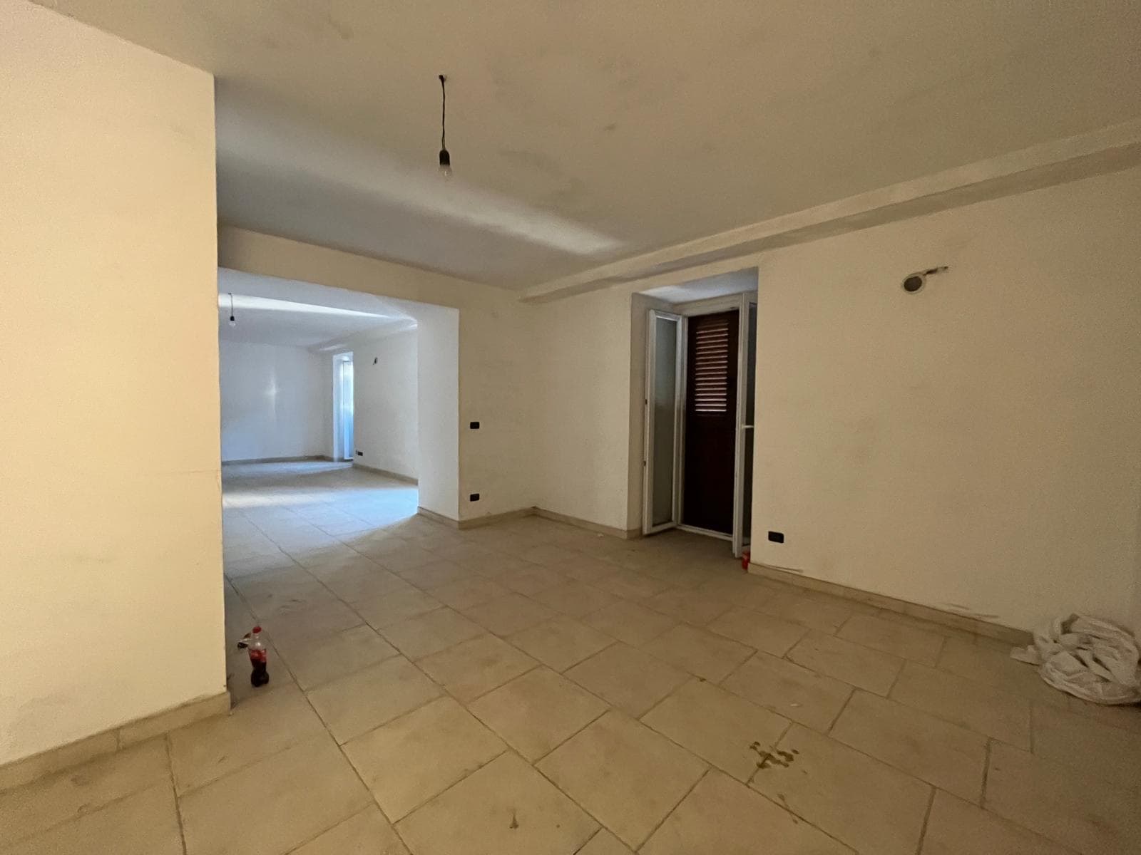 Appartamento in fase di ristrutturazione con pareti bianche e pavimento in piastrelle, ampio soggiorno con accesso a balcone, luce naturale, pronto per personalizzazione e arredo.